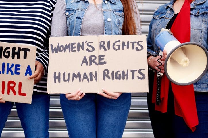 Cropped shot of an unrecognizable woman holding up a poster that reads "Women's rights are human rights" while protesting with other unrecognizable women in the city